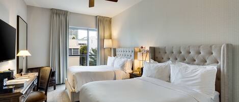 A hotel room with two beds, a desk, a chair, a television, and a ceiling fan.