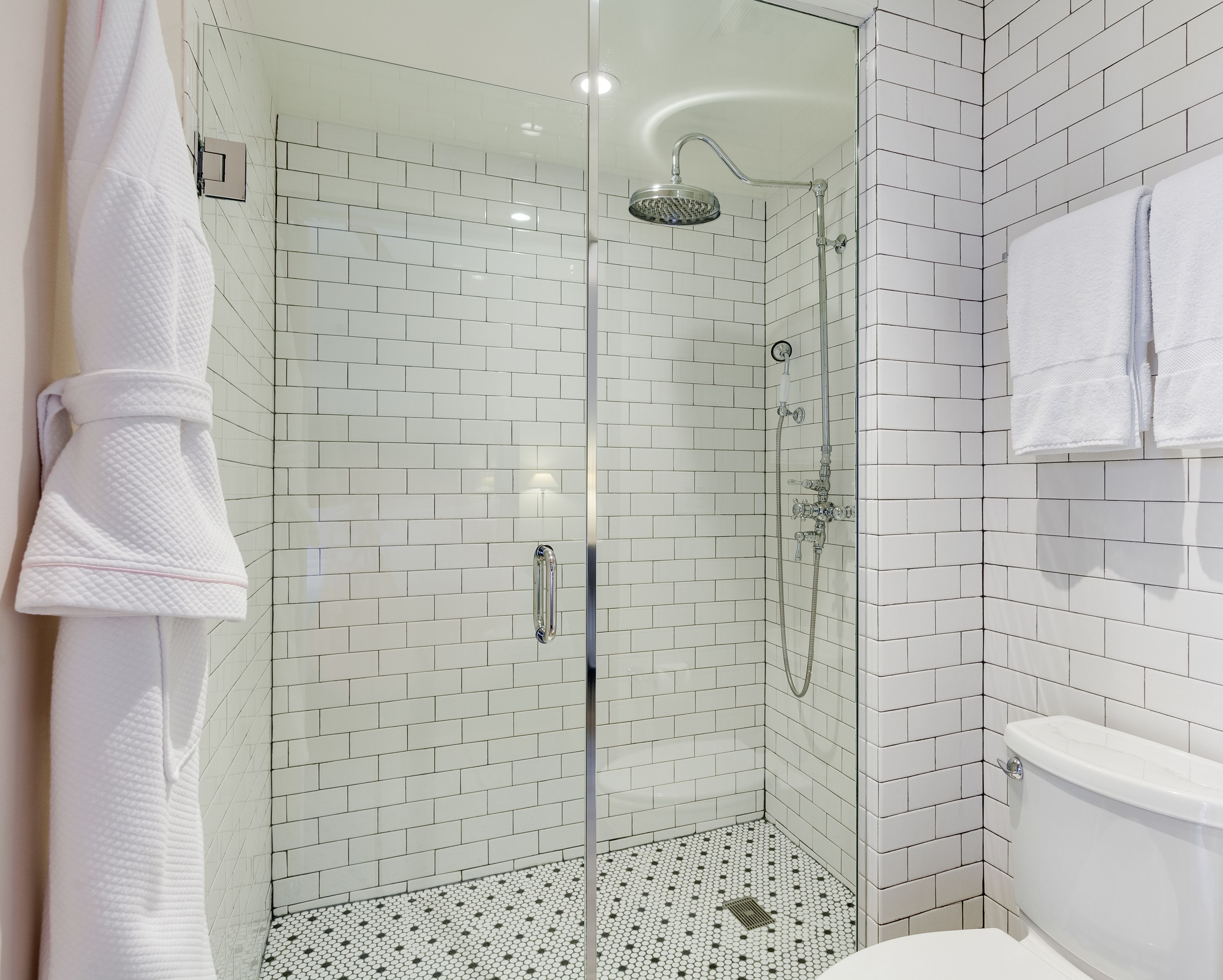 Une salle de bain moderne avec une douche à parois de verre, des murs recouverts de carreaux blancs et des toilettes.