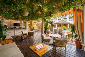 An outdoor patio area with wooden furniture, potted plants, and a pool in the background.
