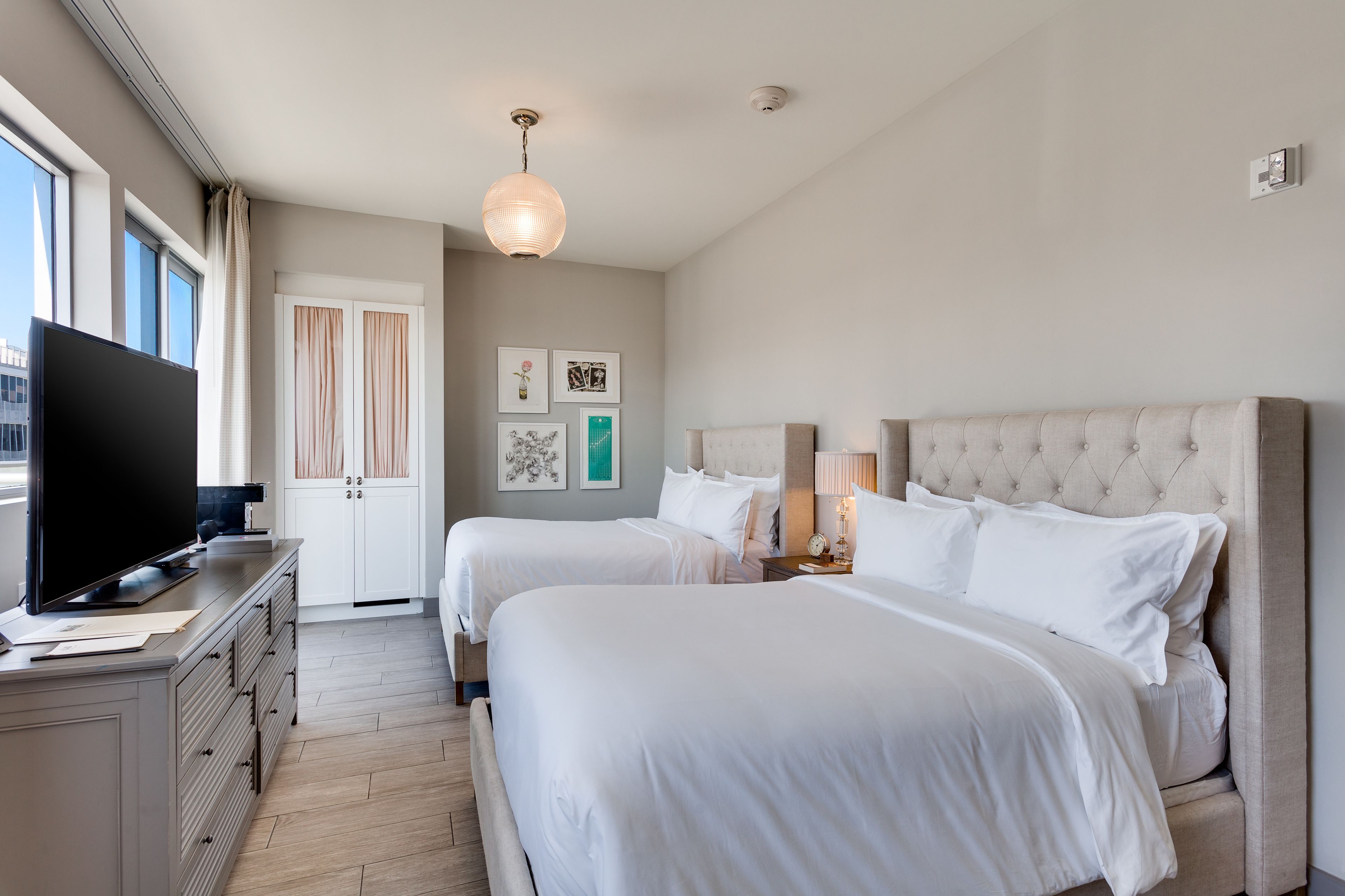 Ein Hotelzimmer mit zwei Betten, einem Fernseher, einem Schminktisch und Bildern an der Wand.
