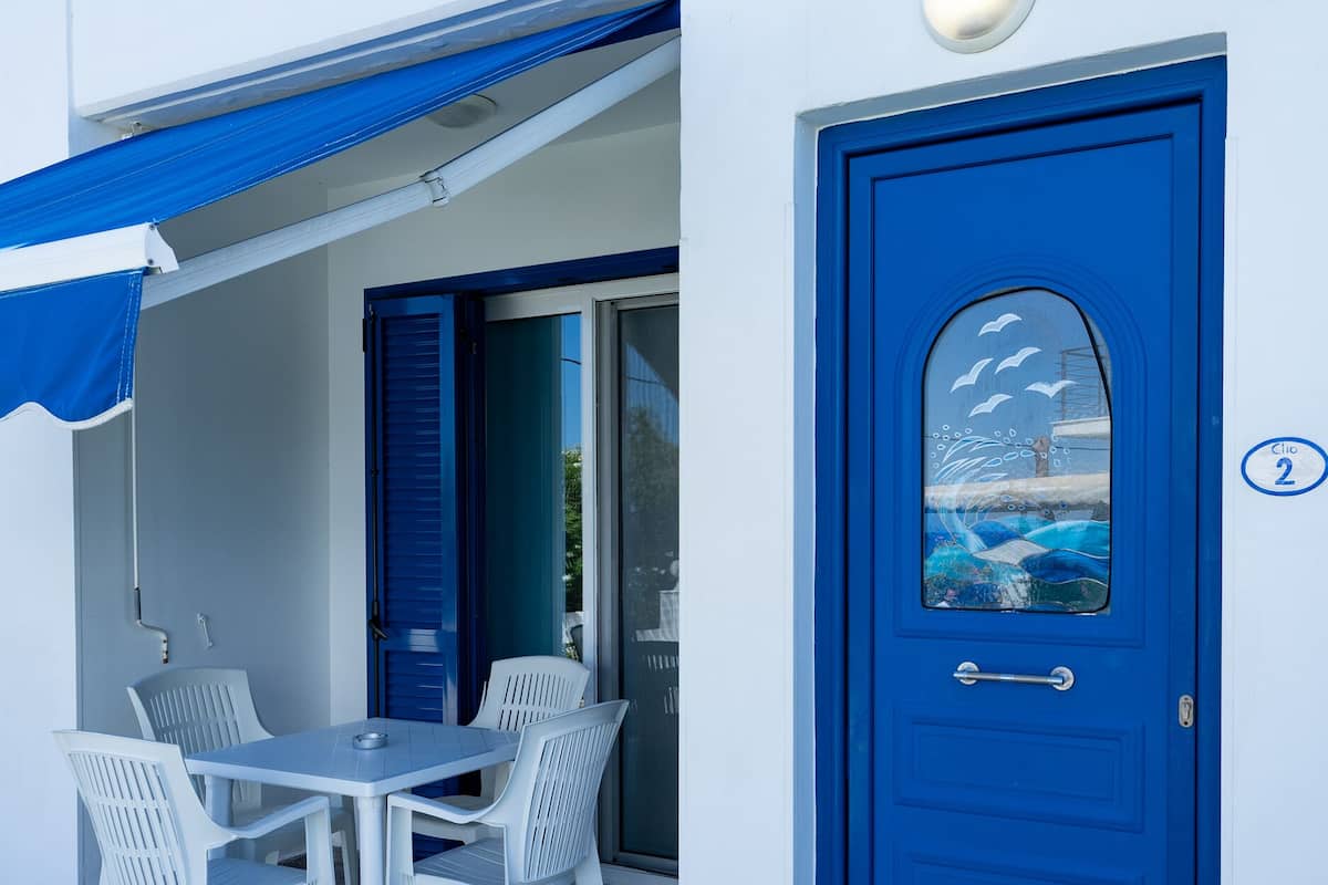 A blue door with a window, a white table with chairs, and a blue awning.