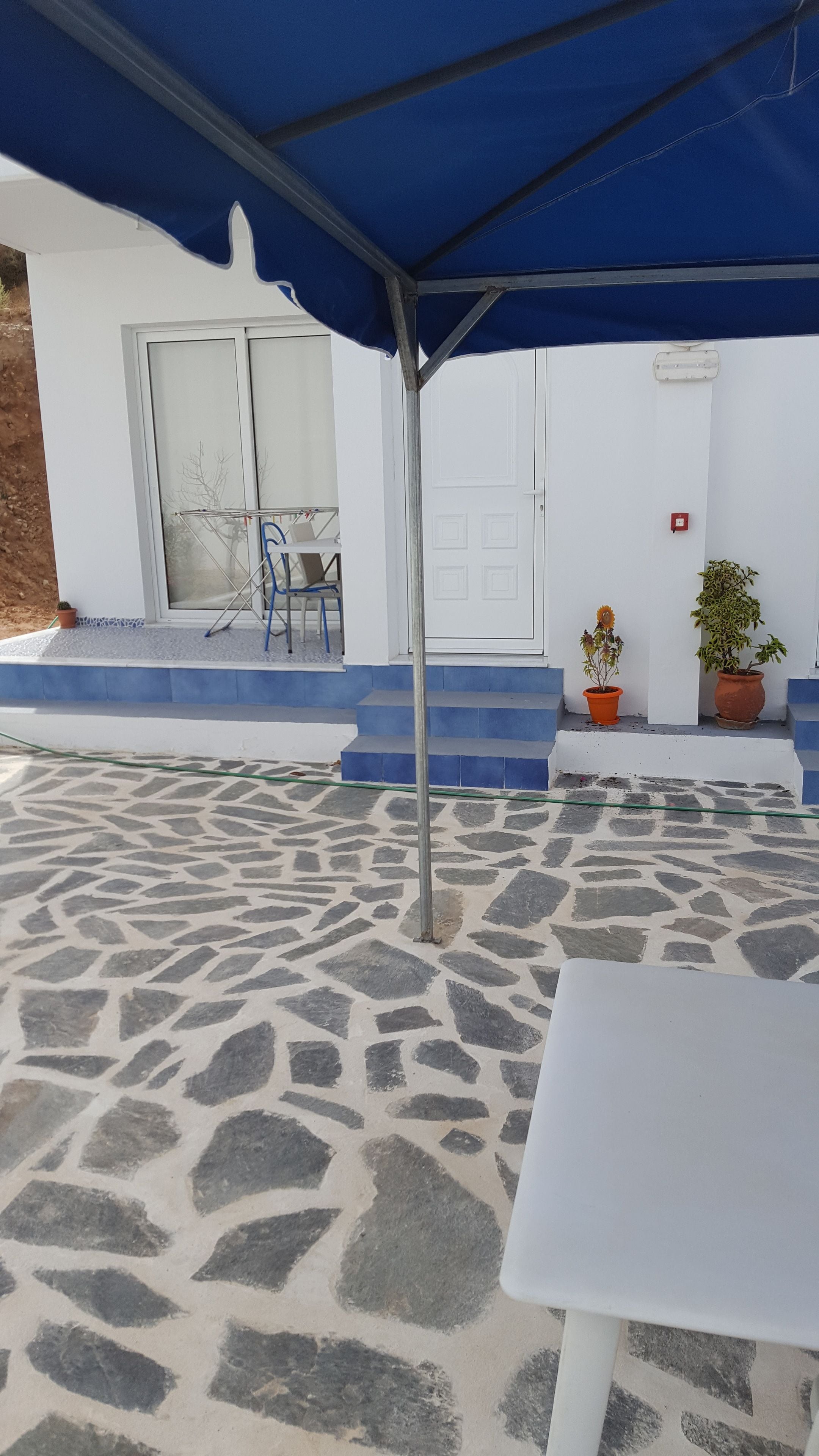 Un espace patio doté d’un sol en pierre, d’une table blanche et d’un auvent bleu.