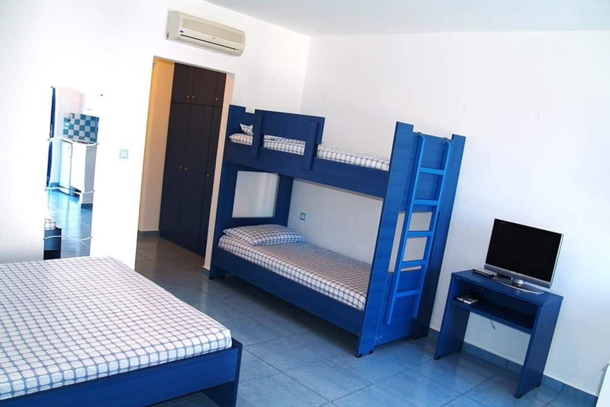 A room with bunk beds, a desk with a TV, and a door leading to another room.