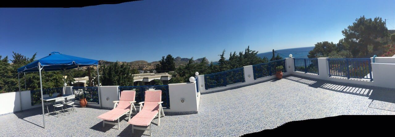 A rooftop terrace with a clear view of the sea, furnished with lounge chairs and a table under a blue canopy.
