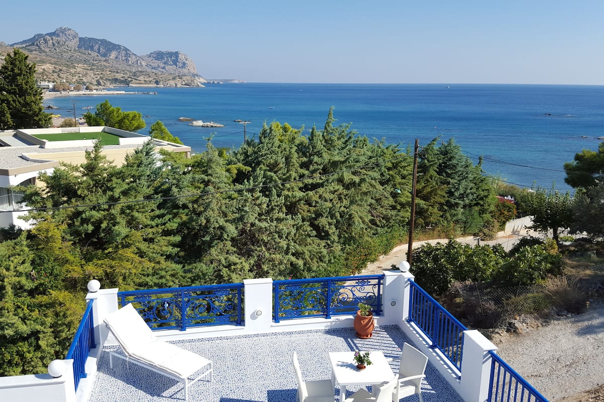 A terrace with a view of the sea, surrounded by trees and buildings.