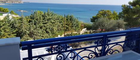 A balcony with a view of the sea, trees, and a distant coastline.