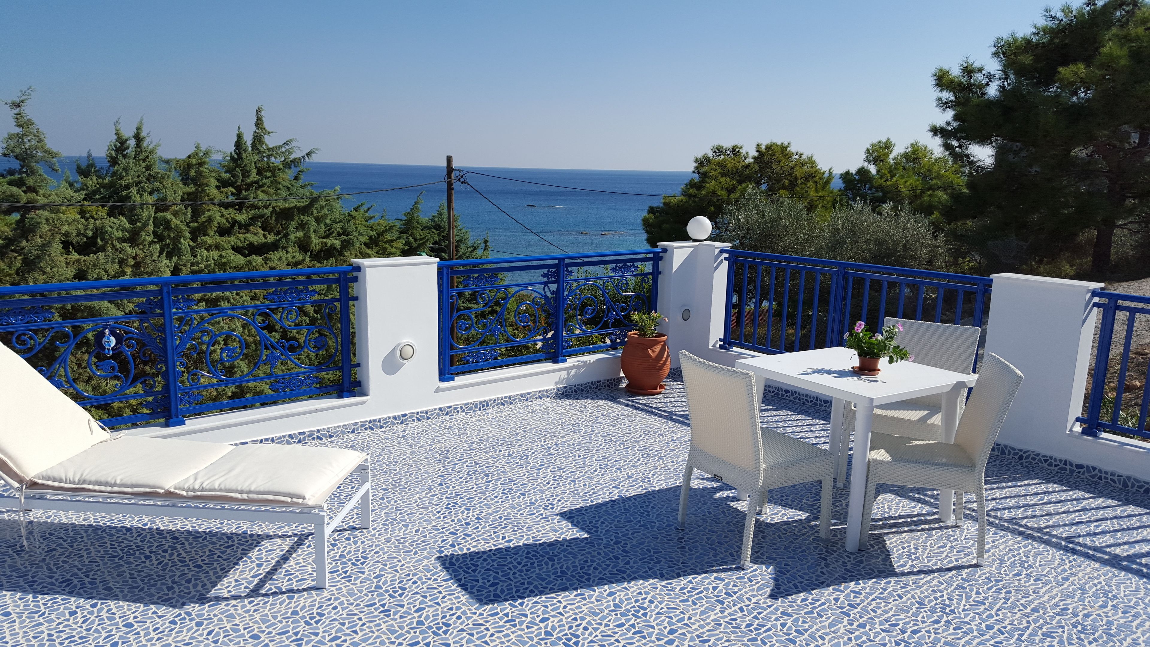 Een terras met wit meubilair, een blauwe reling en uitzicht op zee.