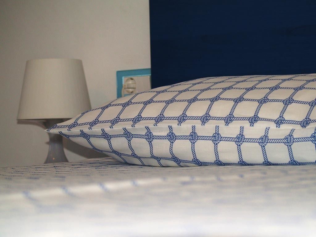 Un lit avec un oreiller à motifs blancs et bleus, une lampe de chevet et un tableau encadré au mur.