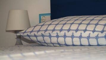 Un lit avec un oreiller à motifs blancs et bleus, une lampe de chevet et un tableau encadré au mur.