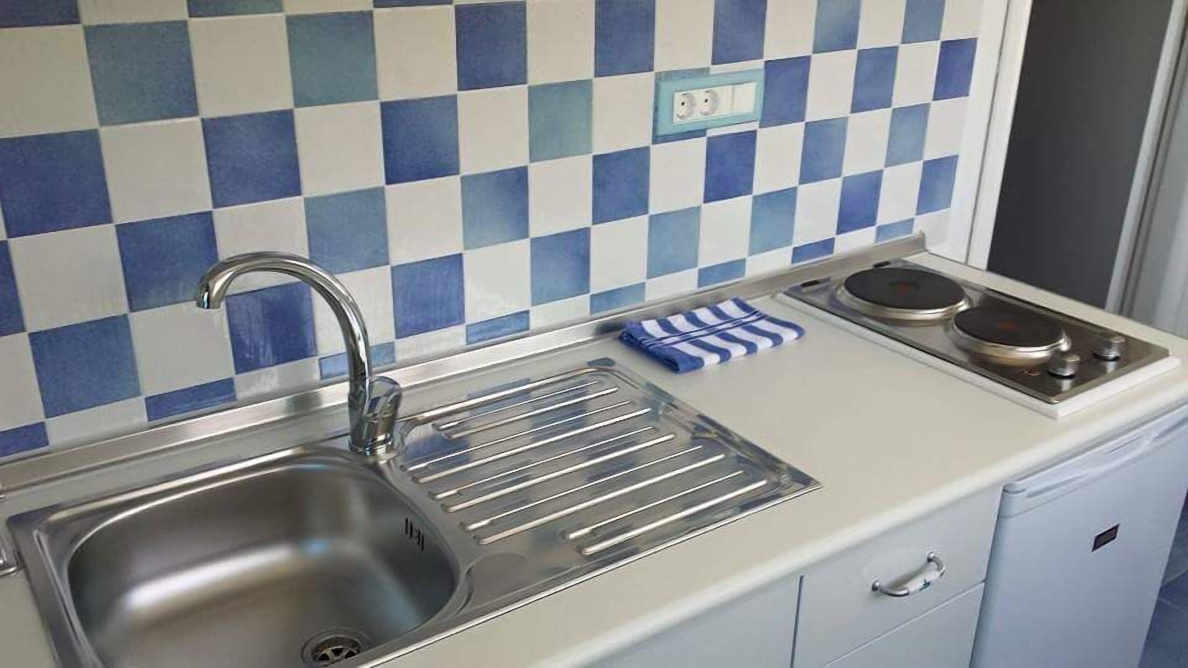 Una cocina compacta con un lavamanos, una hornilla y un salpicadero de azulejos.