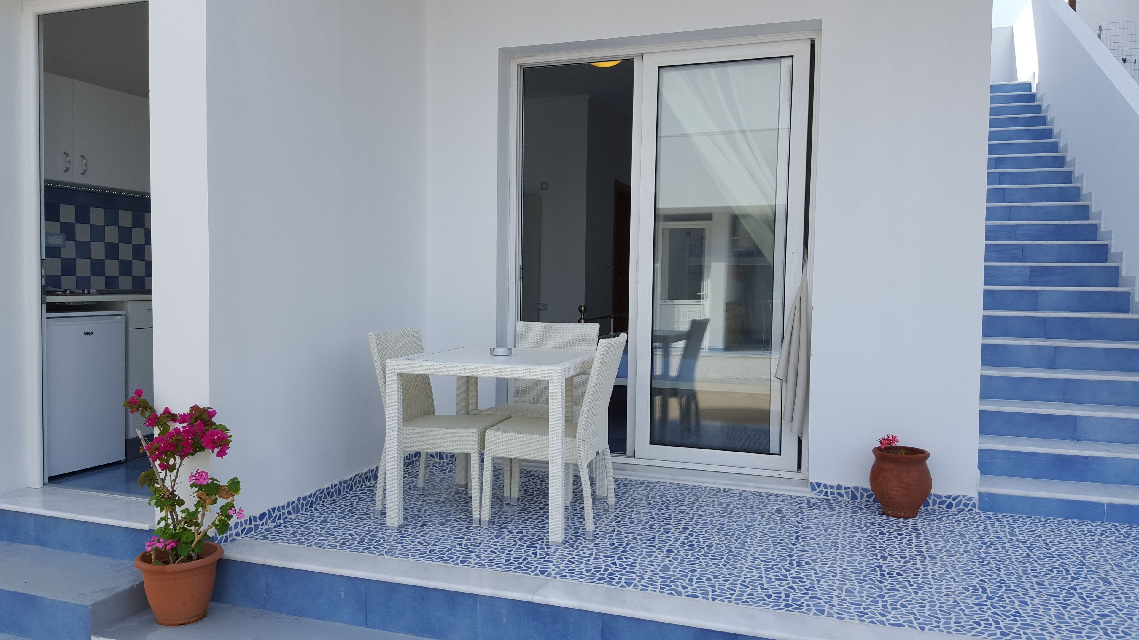 Een balkon met een witte tafel en stoelen, een bloempot en een trap met blauwe treden.