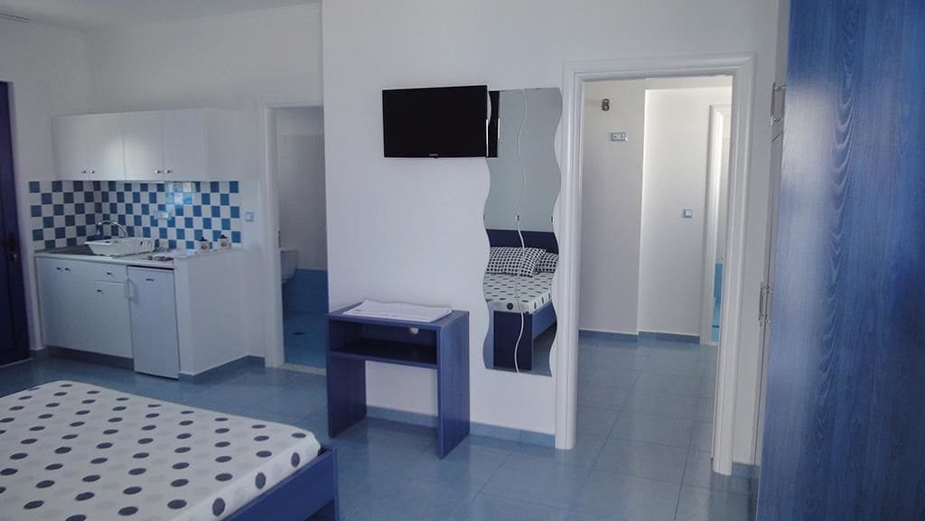 A room with a bed, a desk, a kitchenette, and a TV mounted on the wall.