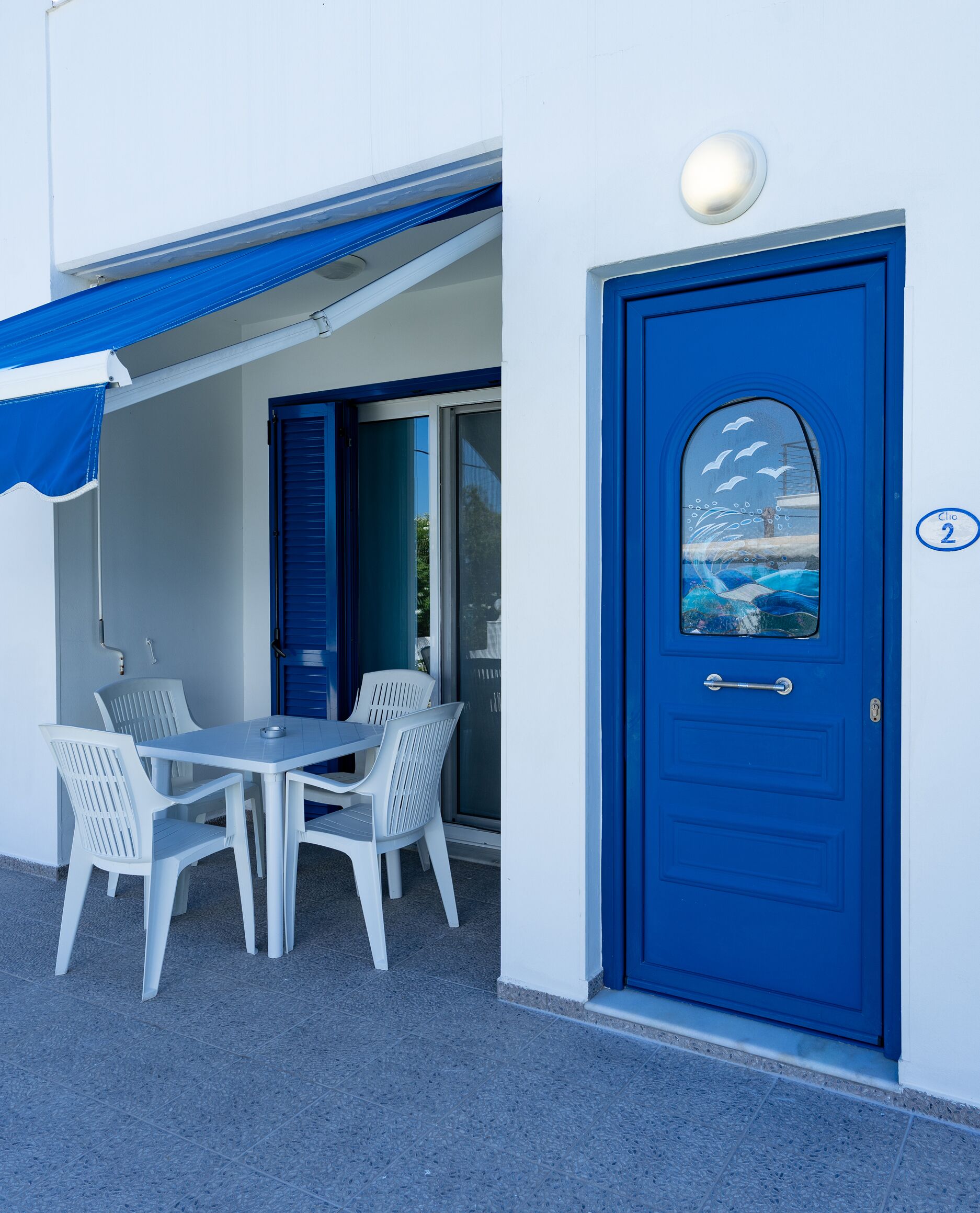 A blue door with a window, a white table with chairs, and a blue awning.