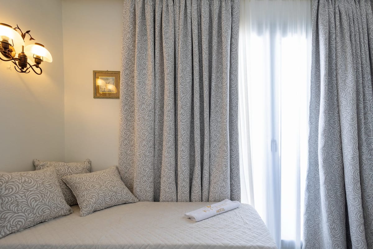 Una cama bien hecha con almohadas estampadas, un cuadro en la pared y una ventana con cortinas.
