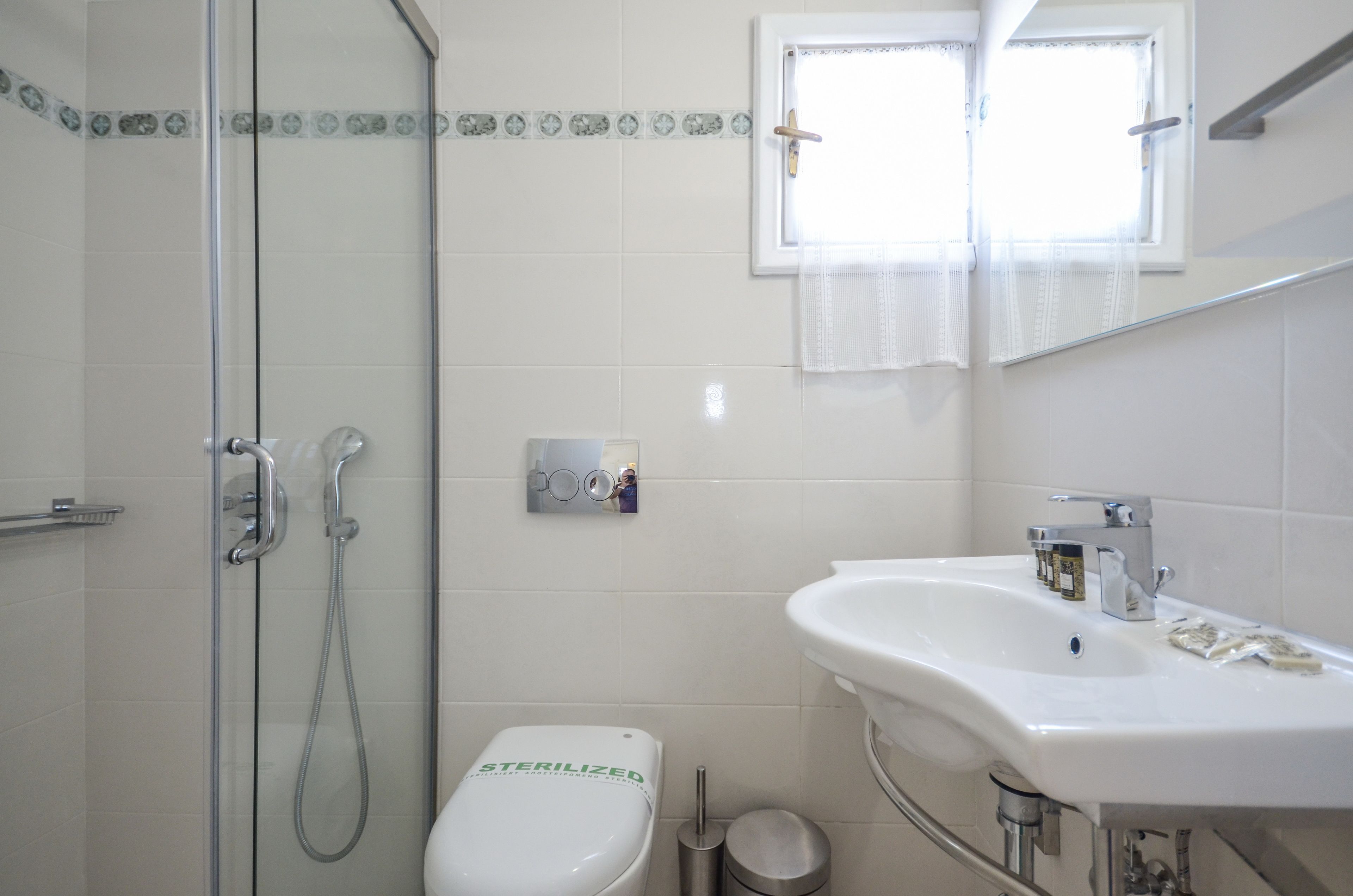A bathroom with a shower, toilet, sink, and a window with curtains.