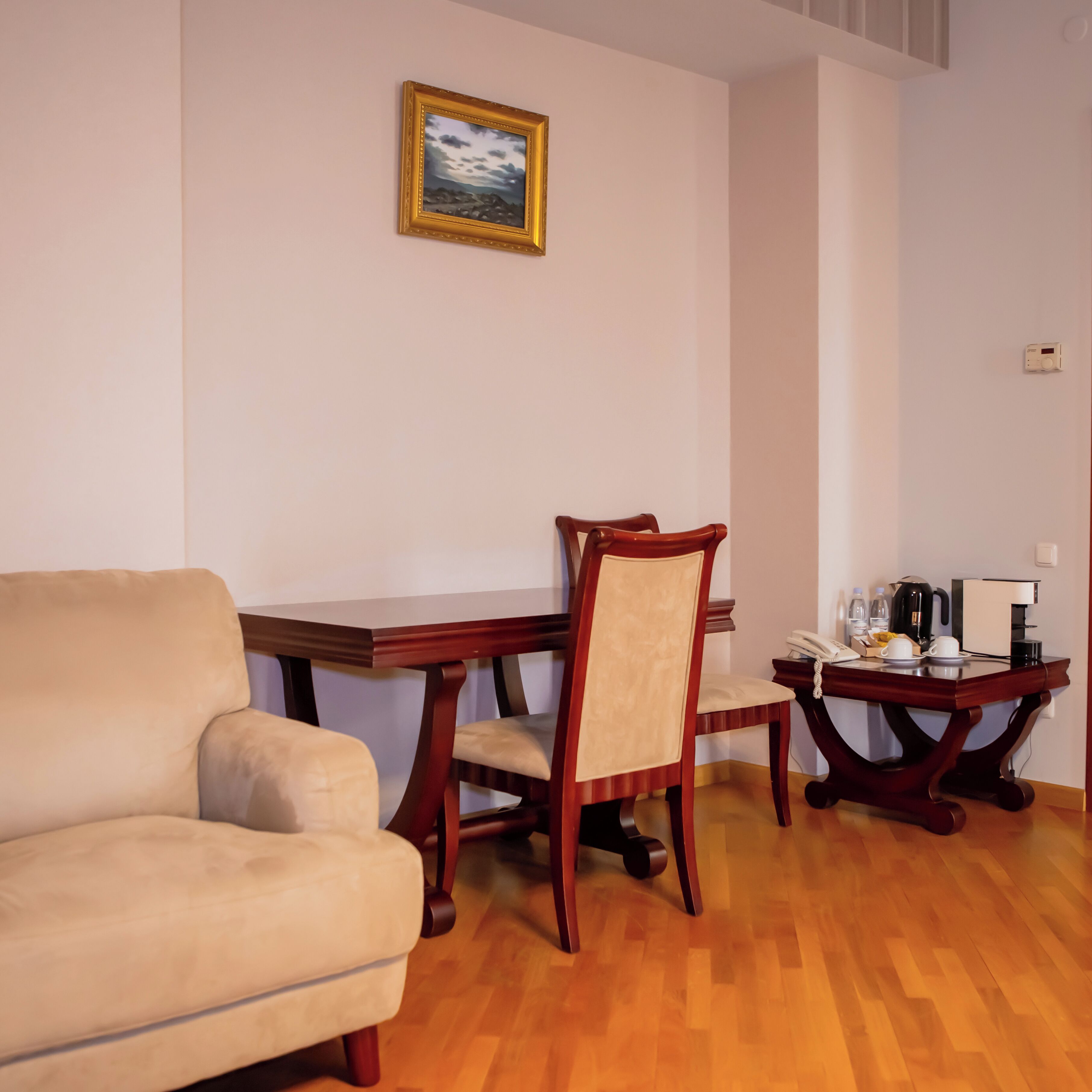 Quarto com uma mesa de jantar de madeira, uma cadeira de madeira, um sofá e uma pequena mesa lateral com uma cafeteira e xícaras.