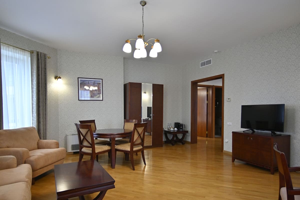 Uma sala de estar com sofá, mesa de jantar com cadeiras, televisão e um armário de madeira.