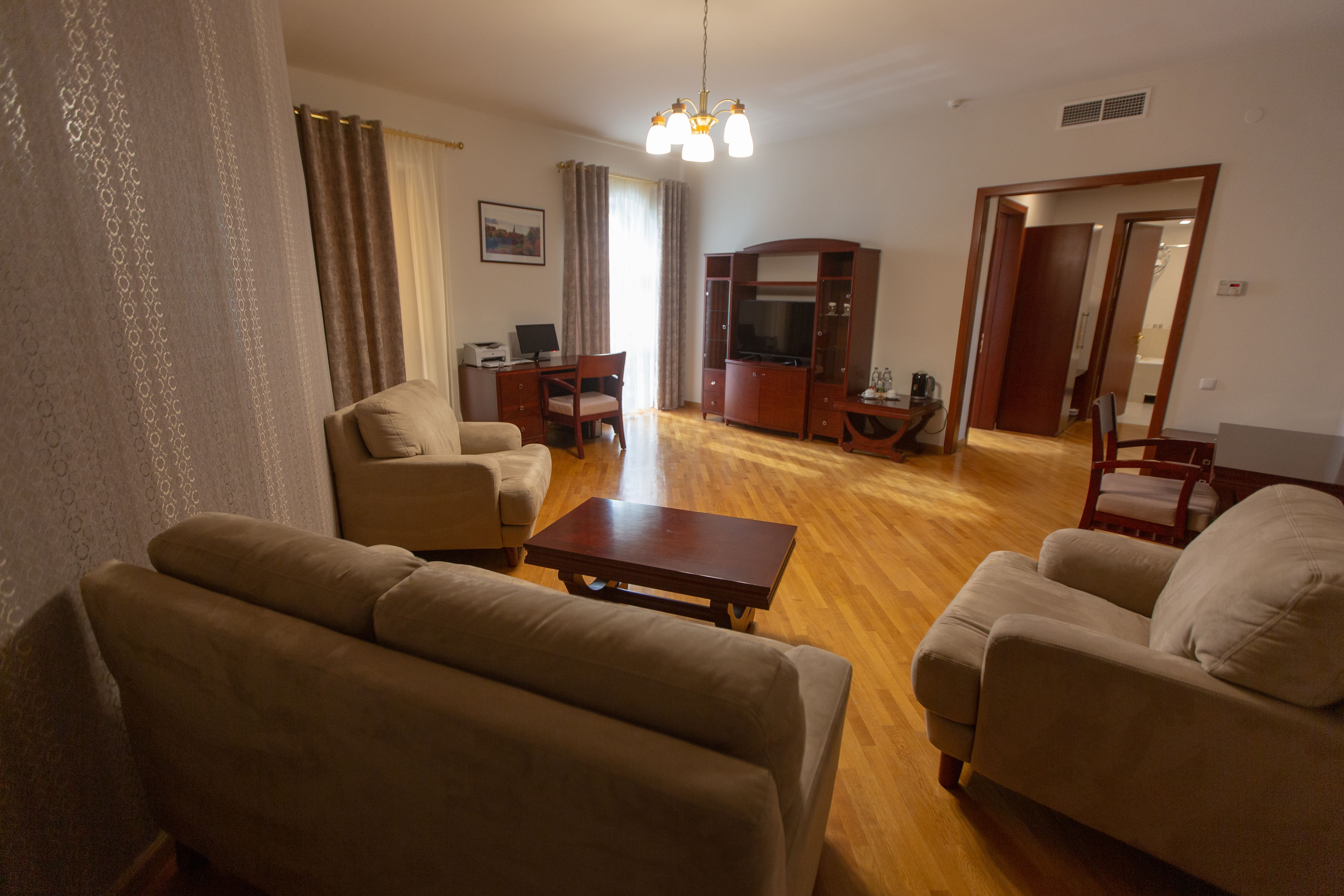 A living room with a sofa, armchairs, a coffee table, a TV, and a desk with a computer.