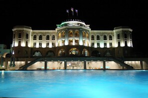 A large hotel with a swimming pool in front, featuring multiple balconies and a grand entrance.
