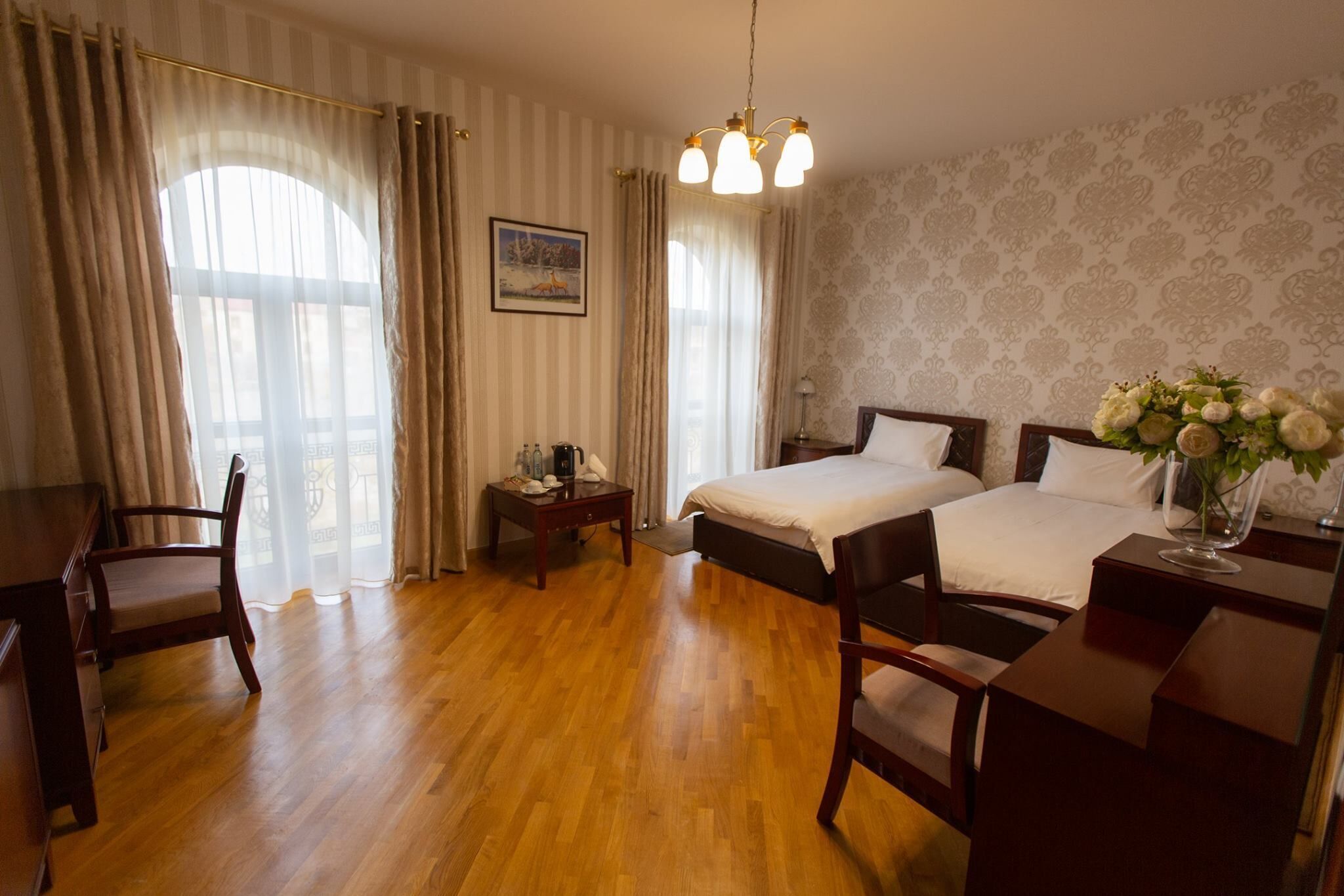 A hotel room with two beds, wooden furniture, a desk, and a chandelier.