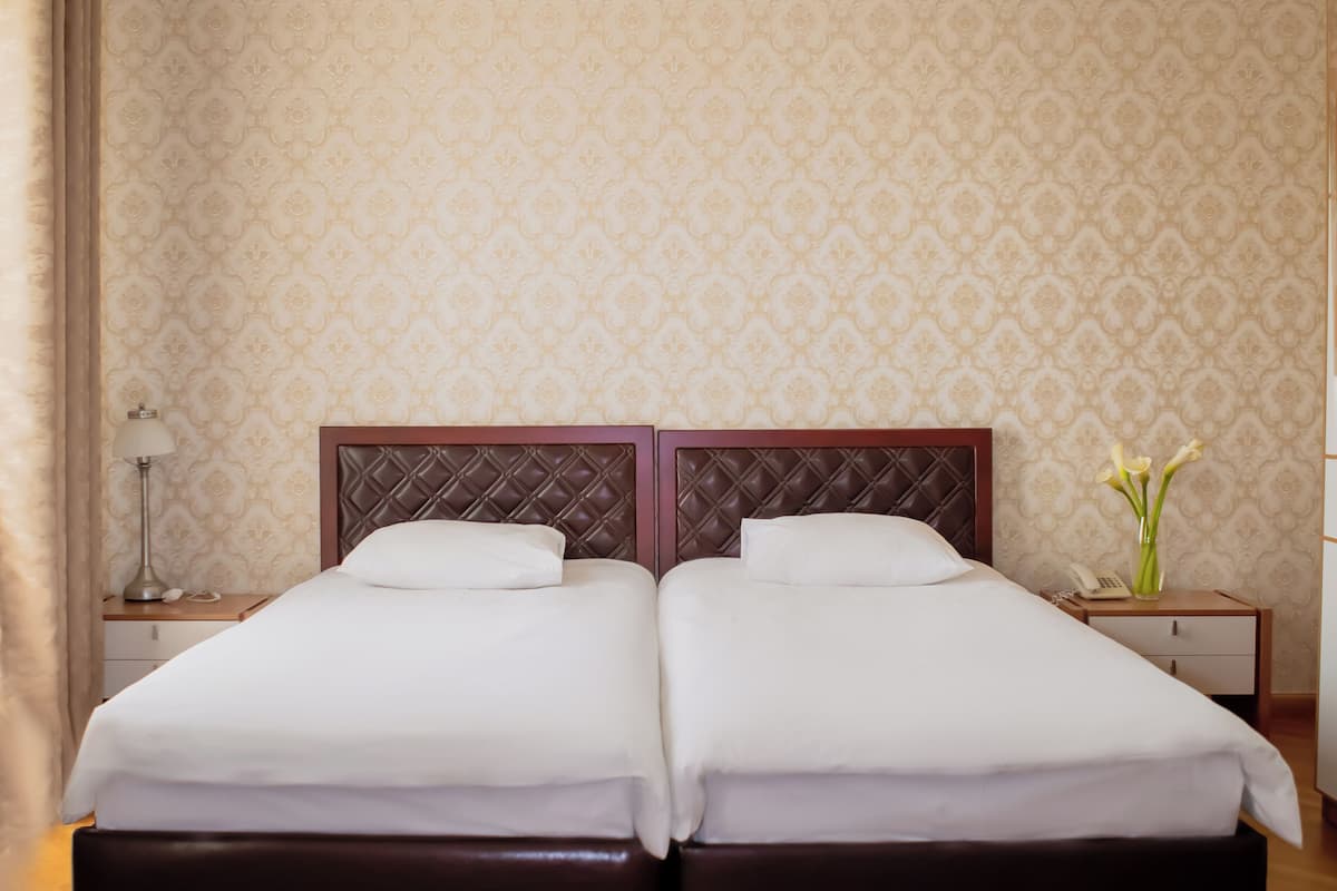 Uma cama de casal com cabeceira de madeira, uma mesa de cabeceira com abajur e um vaso com flores no criado-mudo.