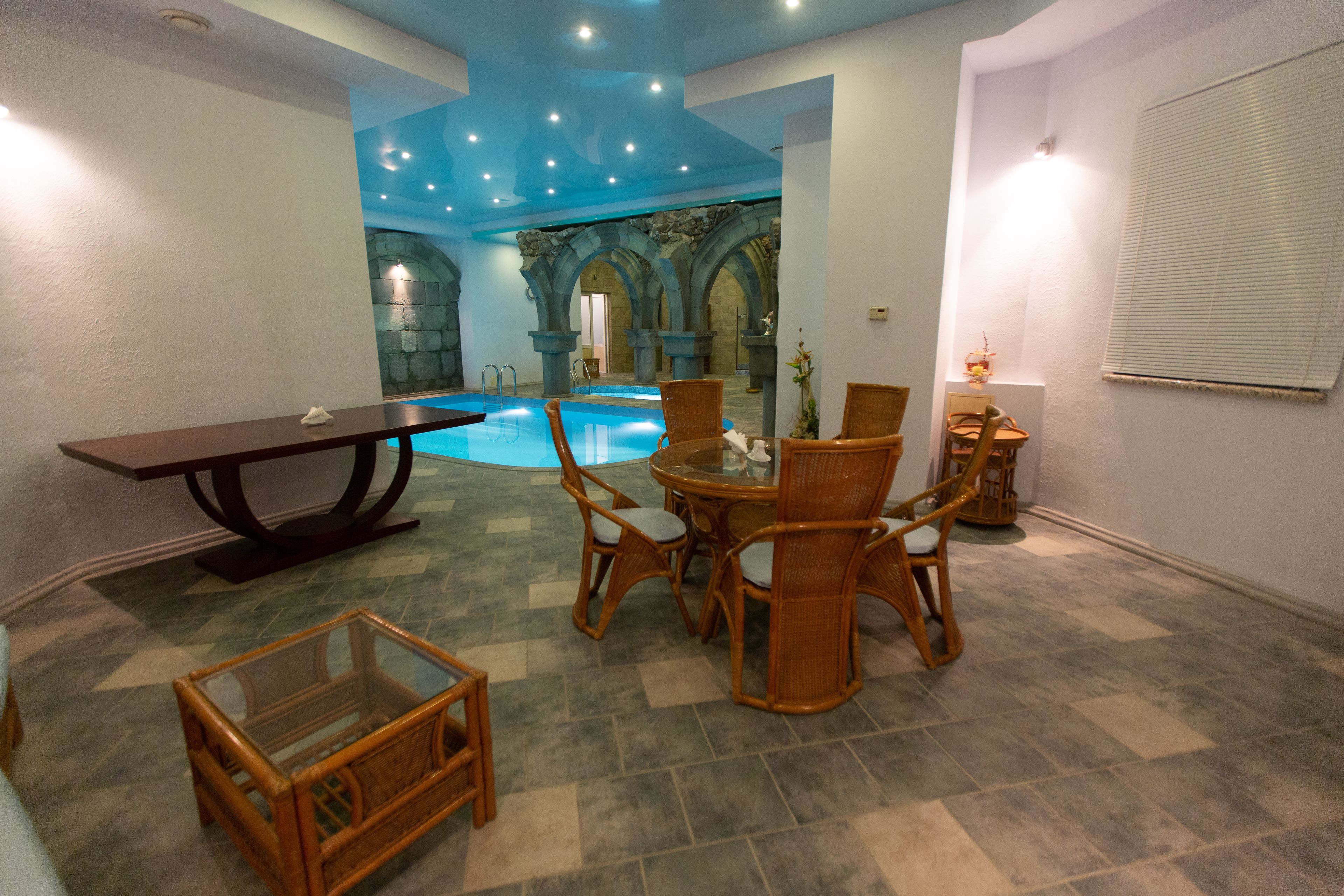 A pool area with a table and chairs, stone arches, and a tiled floor.