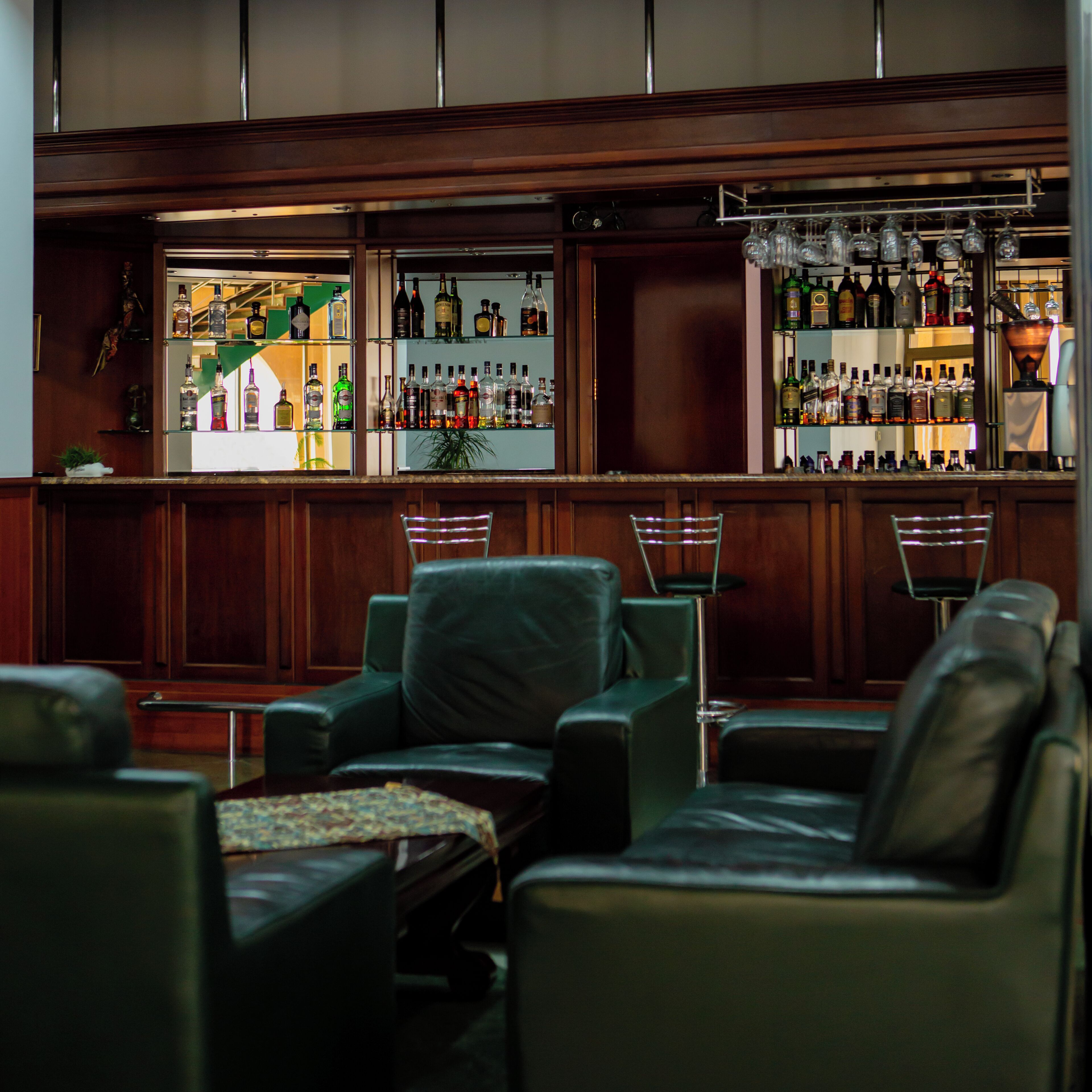 A bar area with leather seating, a bar counter stocked with liquor bottles, and a hanging light fixture.