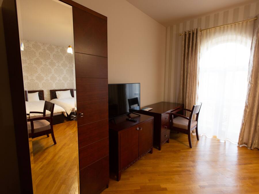 Une chambre d’hôtel avec un plancher en bois, un bureau avec une télévision, une chaise et un lit avec du linge de lit blanc.