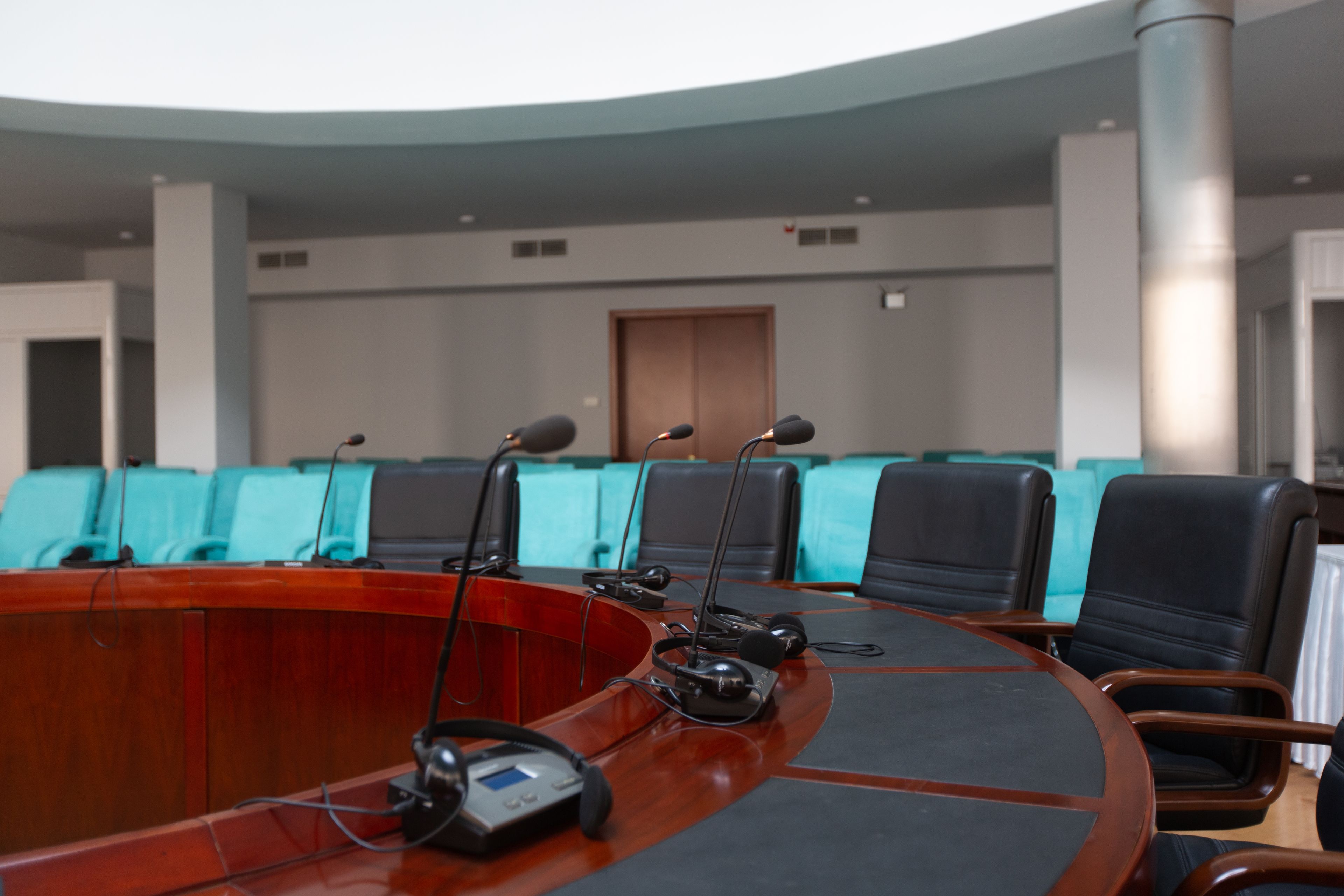 A conference room with a curved table, multiple microphones, and chairs.