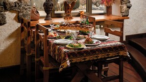 A dining area with a stone arch window overlooking a scenic view, wooden furniture, and a table set for a meal. - Latar Hotel Complex (Yerevan)