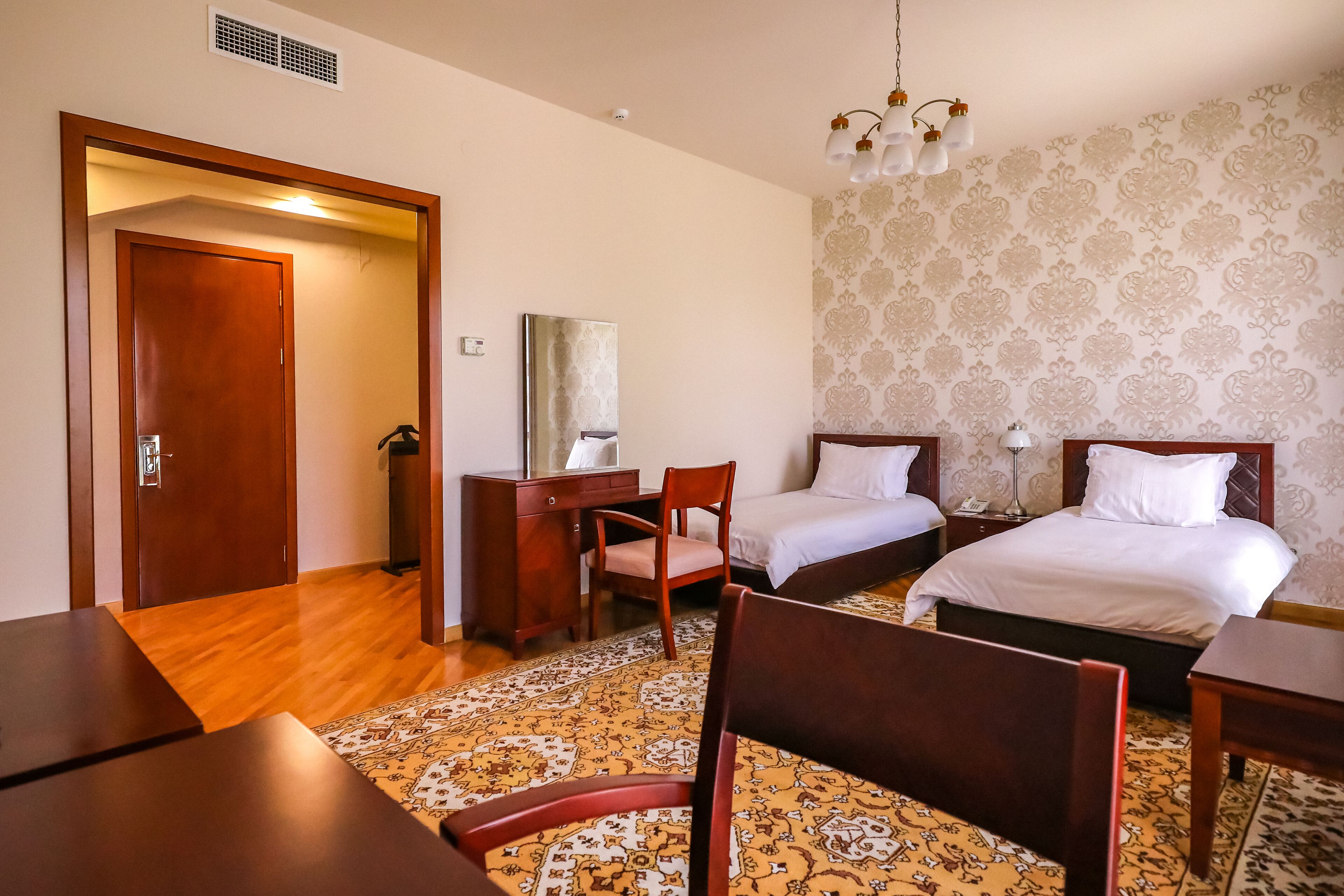 Habitación de hotel con dos camas, un escritorio, una silla, un espejo y una alfombra estampada.