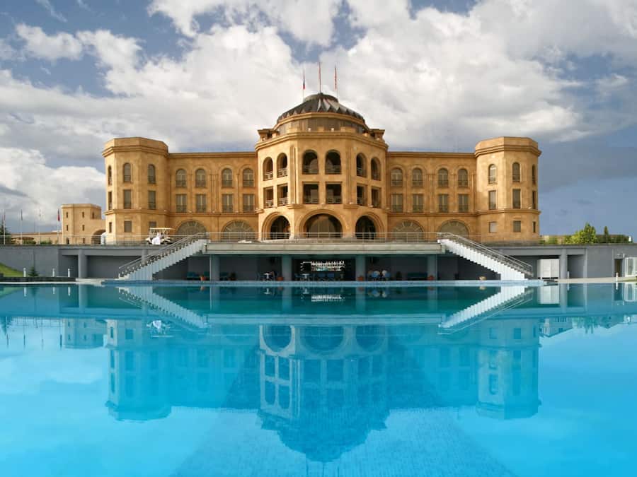A large building with a central dome and arched windows, reflecting in a pool in front.