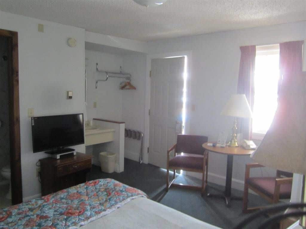 Une chambre d’hôtel comprenant un lit, une télévision, un bureau avec une lampe, une chaise et une fenêtre avec des rideaux.