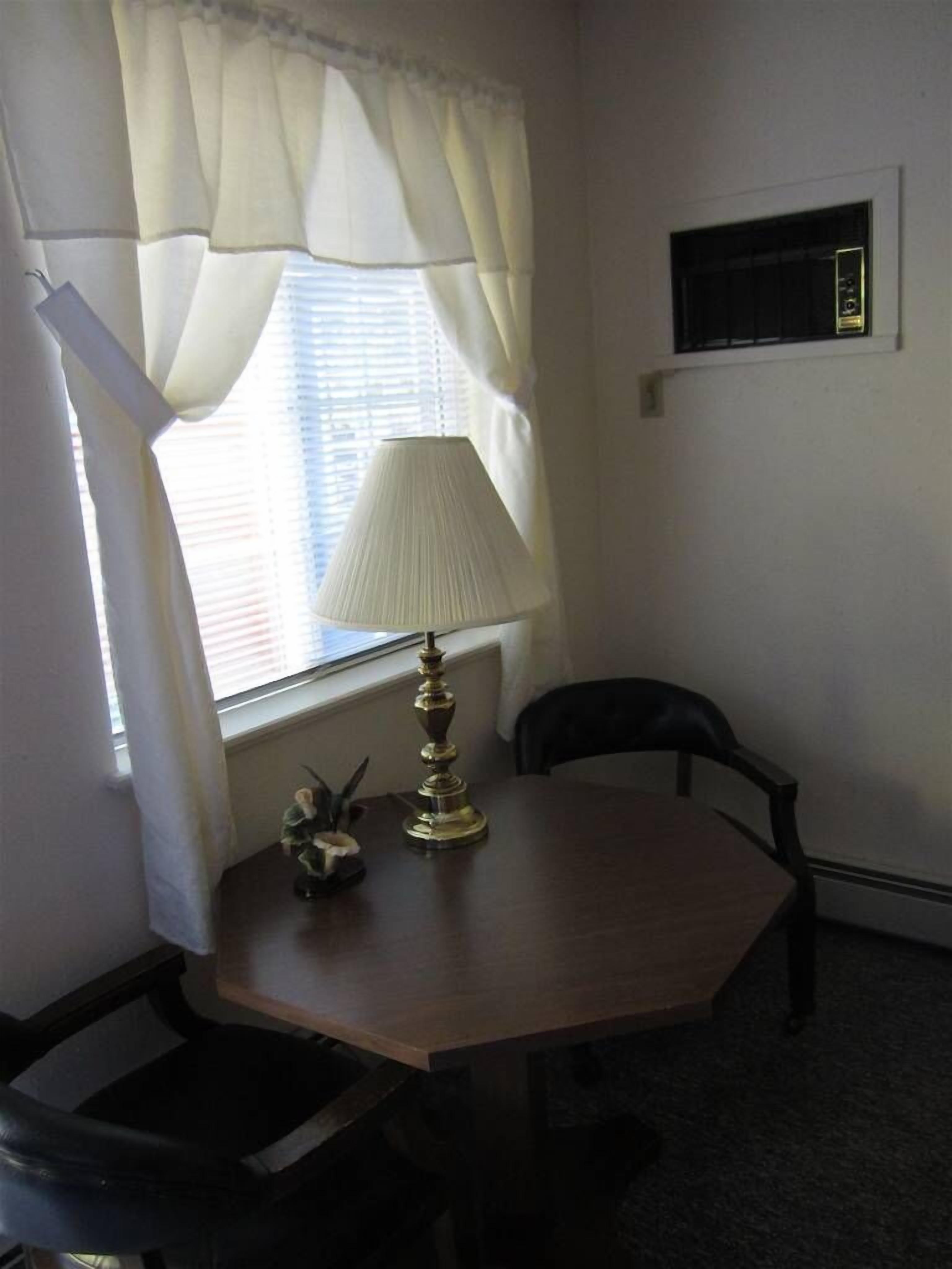 A small room with a table, a chair, a lamp, and a window with curtains.