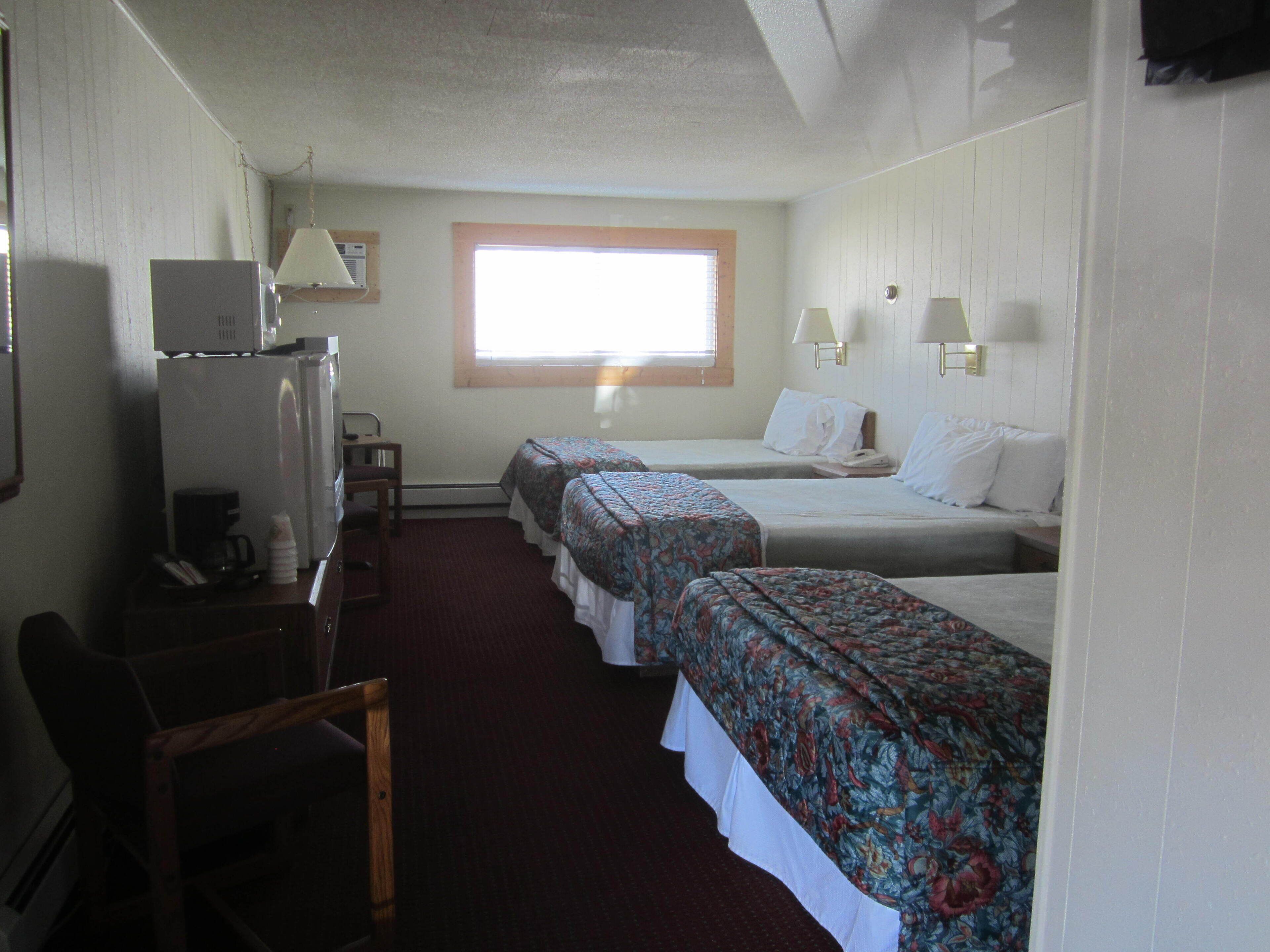 A hotel room with two beds, a desk with a computer, a chair, and a window with blinds.