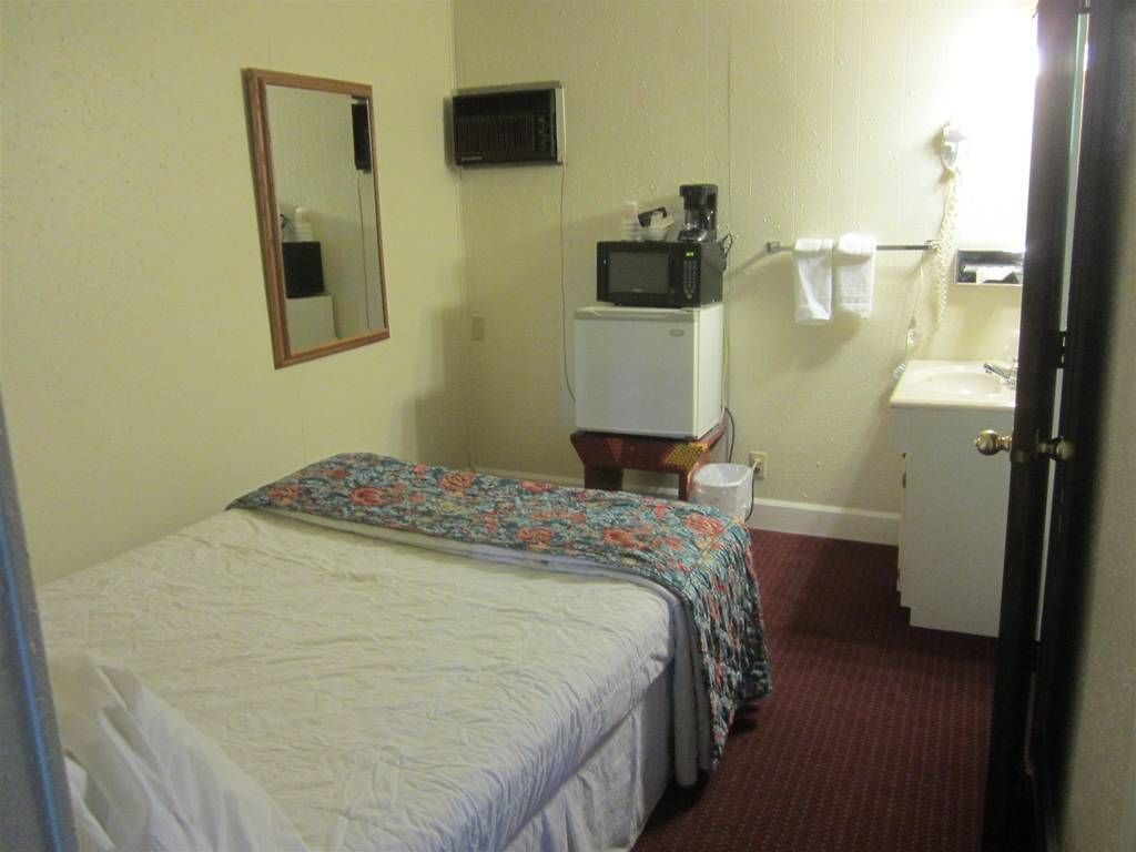 A hotel room with a bed, a small kitchenette with a microwave and coffee maker, a sink, and a mirror.