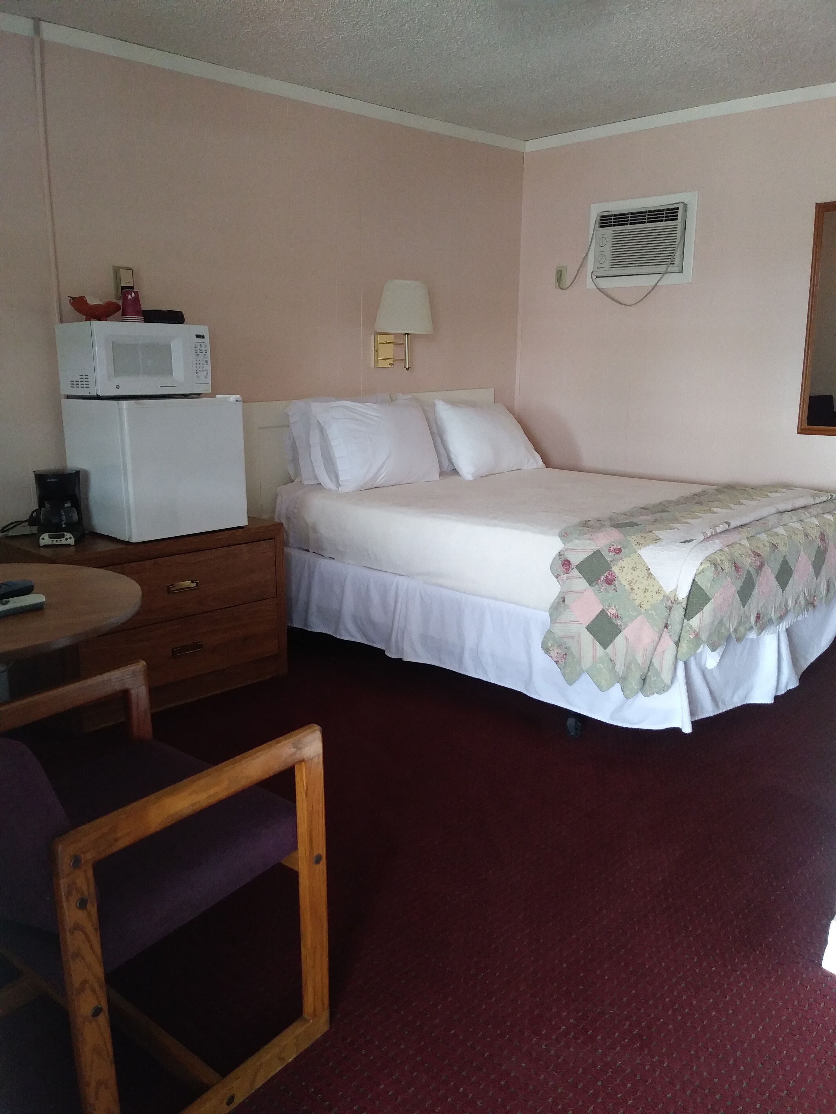 Une chambre d’hôtel équipée d’un lit, d’un bureau avec une chaise, d’un four à micro-ondes, d’une machine à café et d’une lampe fixée au mur.
