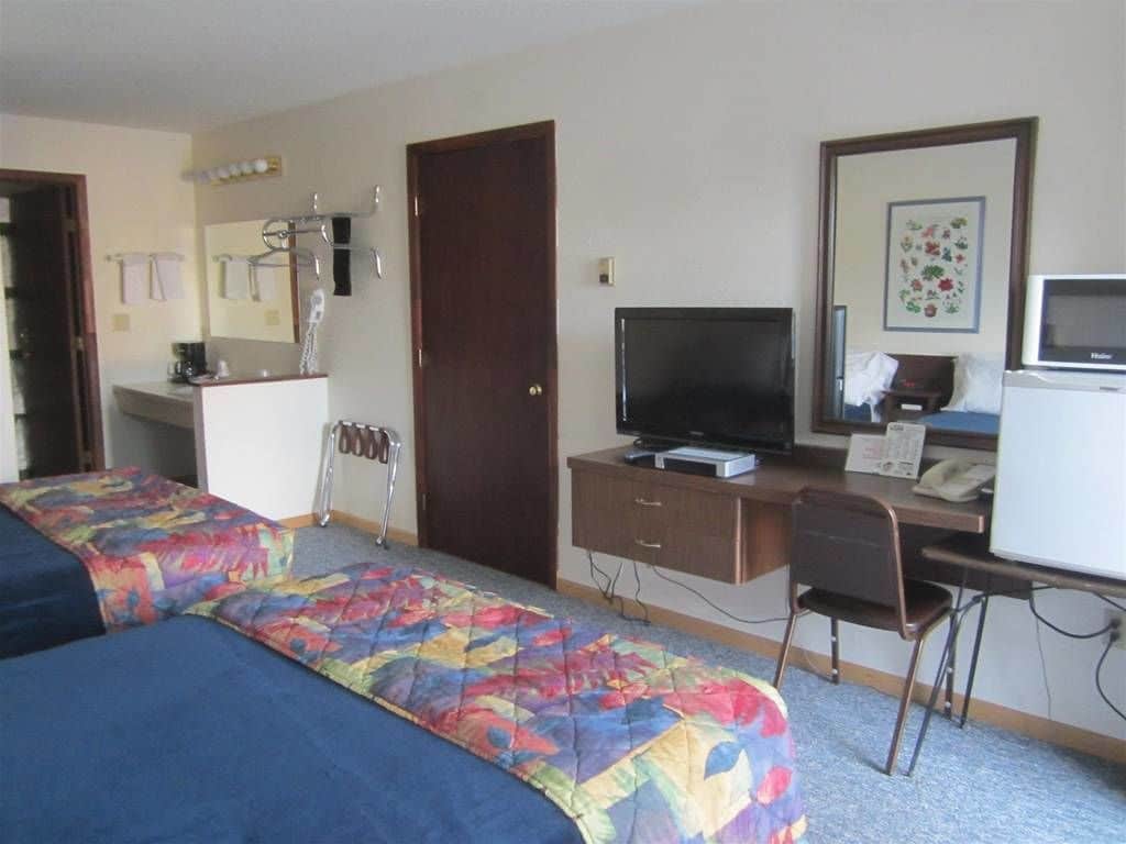Een hotelkamer met twee bedden, een bureau met een computer, een televisie en een magnetron.