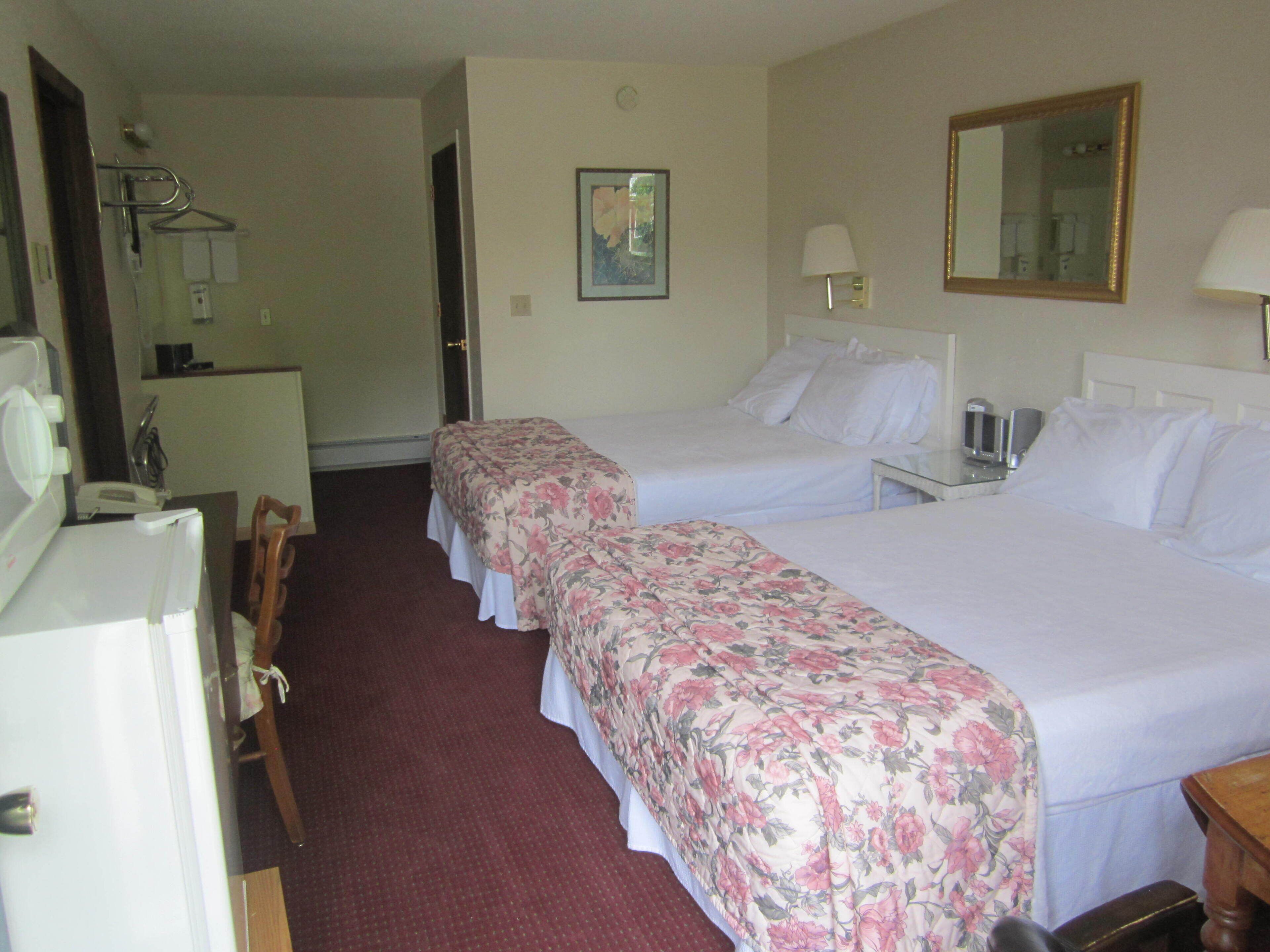 A hotel room with two beds, a desk, a chair, a mirror, and a small table with a lamp.