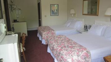 A hotel room with two beds, a desk, a chair, a mirror, and a small table with a lamp.