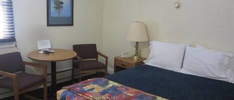 Une chambre d’hôtel avec un lit, un bureau avec une chaise, une lampe et un tableau encadré au mur.