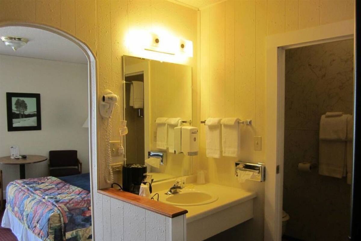 Casa de banho de hotel com lavatório, espelho e dispensador de toalhas.