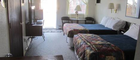 A hotel room with two beds, a desk, a chair, a lamp, and a window with curtains.