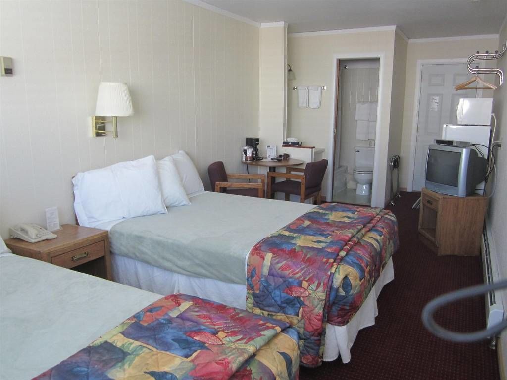 Habitación de hotel con dos camas, un escritorio, una silla, un televisor y la puerta del baño.