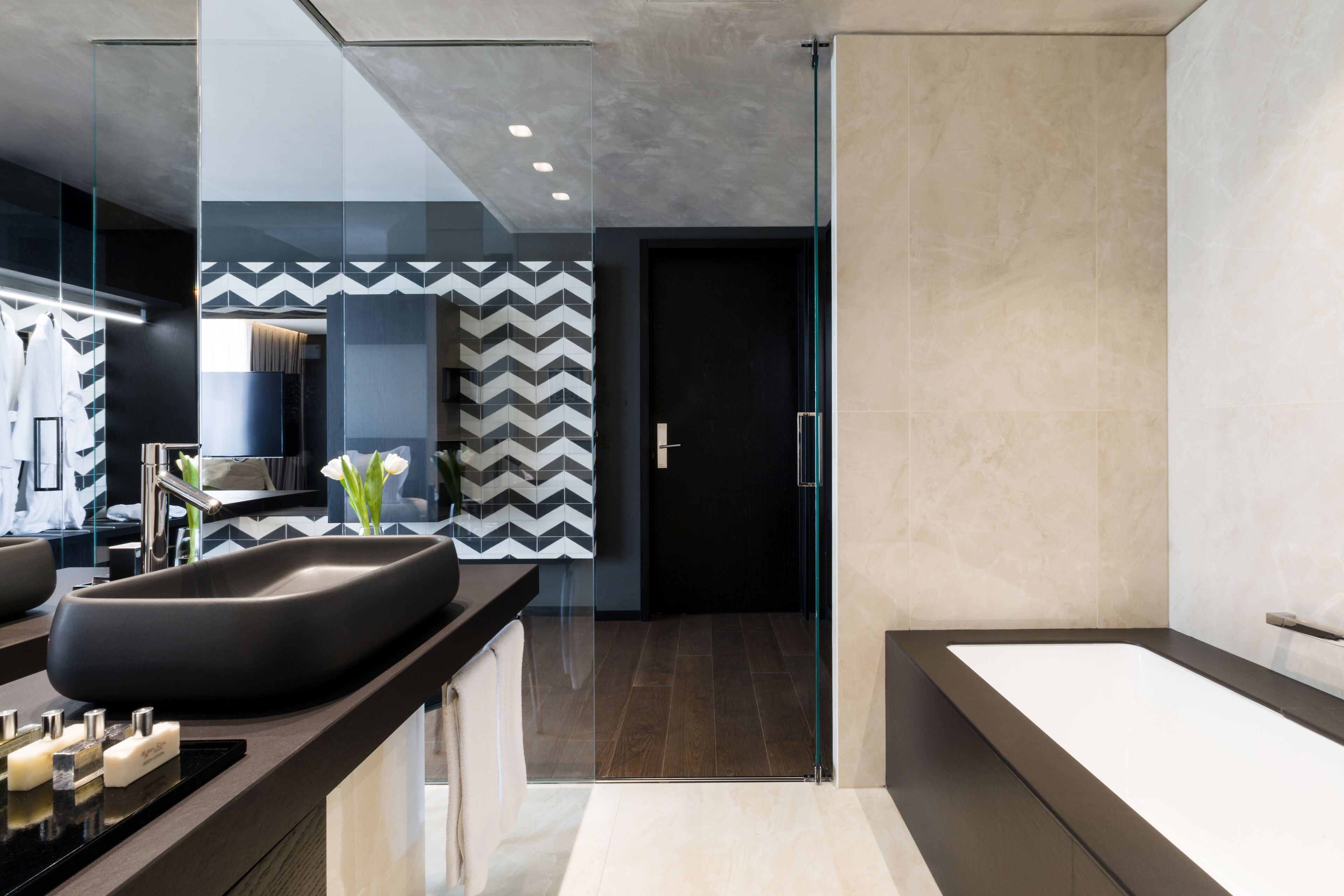 A modern bathroom with a large black sink, a glass shower enclosure, and a beige tiled floor.