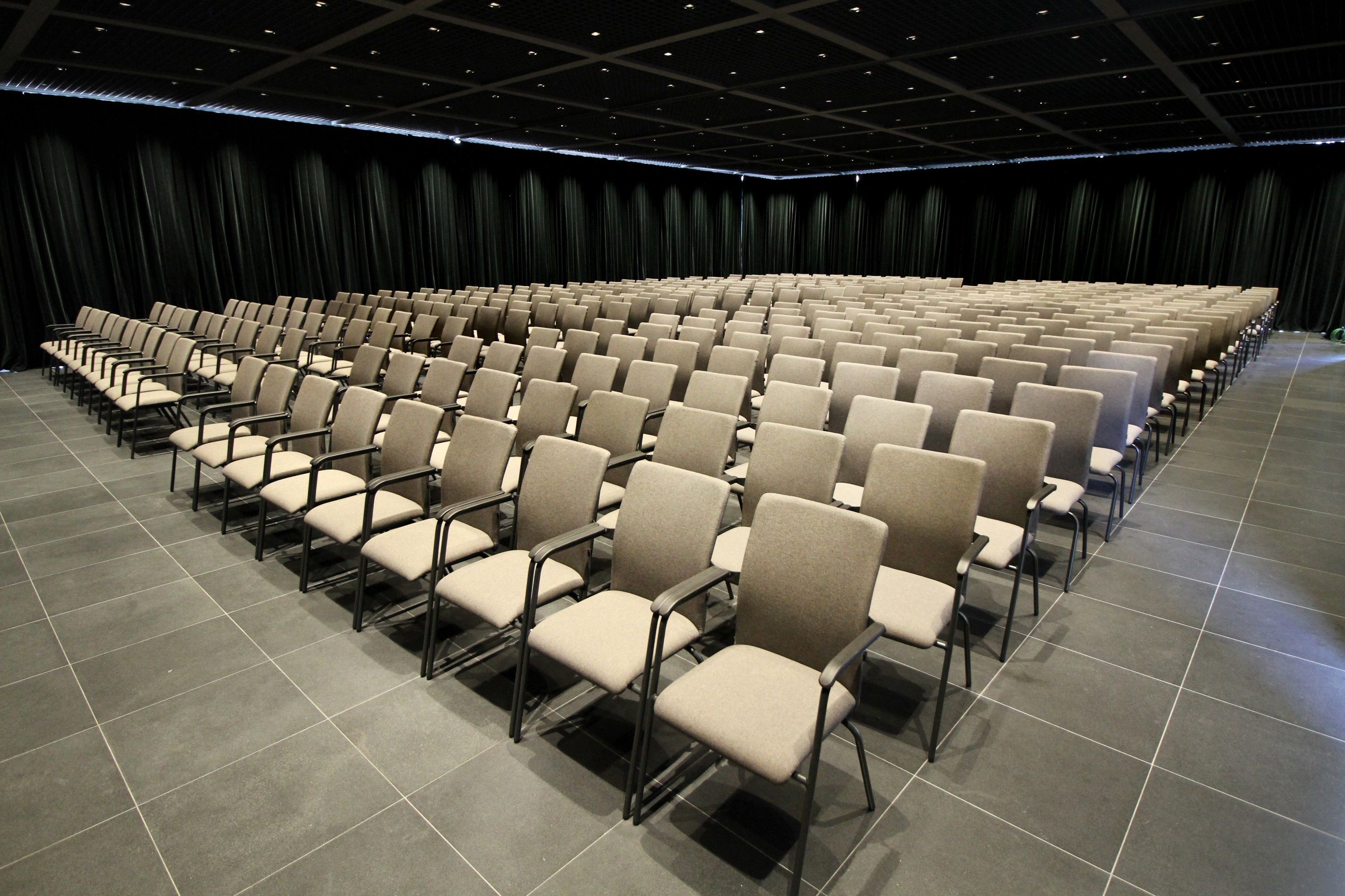 Ein großes, modernes Auditorium mit Reihen beigefarbener Sessel und einem dunklen Vorhang im Hintergrund.