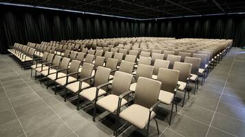 Ein großes, modernes Auditorium mit Reihen beigefarbener Sessel und einem dunklen Vorhang im Hintergrund.