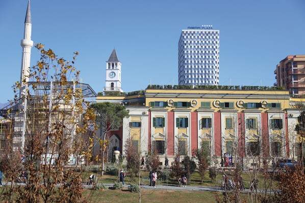 A historic building with a clock tower, a modern high-rise, and a park with people.
