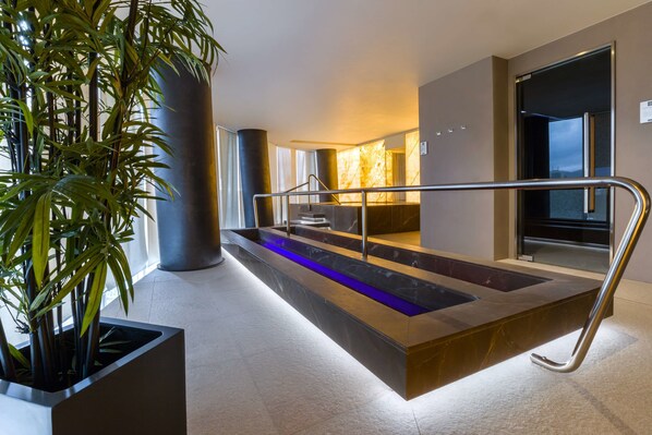 Un moderno vestíbulo de hotel con un mostrador de recepción de mármol, una fuente iluminada en azul y una gran planta en maceta.