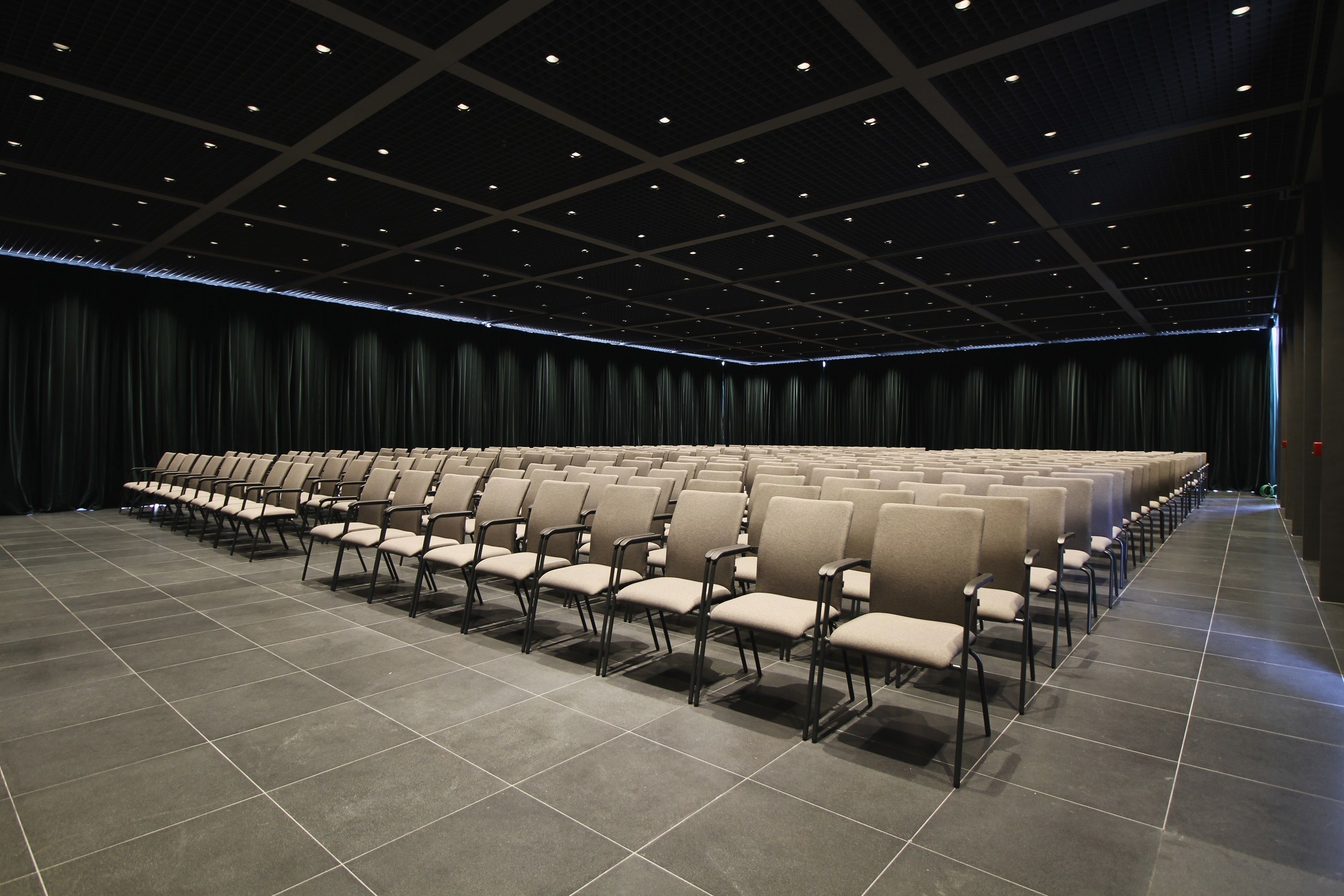 A large, empty auditorium with rows of chairs and a dark, patterned ceiling.